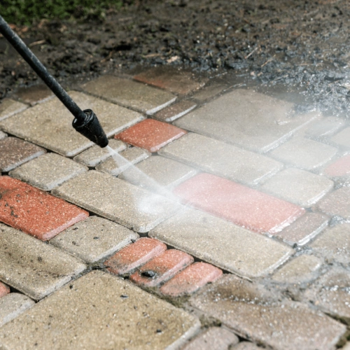 A man using a pressure washer to clean a brick walkway.